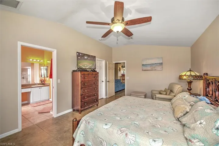 Tiled bedroom featuring ceiling fan, vaulted ceiling, sink, and ensuite bath