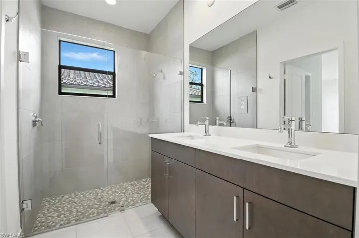 Bathroom featuring a shower stall, double vanity, plenty of natural light, and tile patterned floors