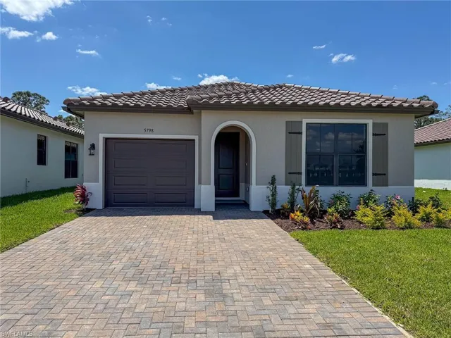 Mediterranean / spanish home with stucco siding, decorative driveway, a front yard, a garage, and a tiled roof