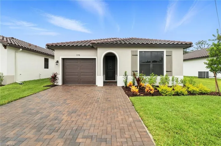 Mediterranean / spanish-style home with decorative driveway, stucco siding, a front yard, an attached garage, and a tile roof