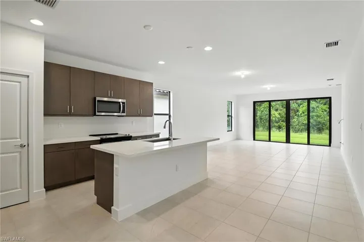 Kitchen with stainless steel microwave, range with electric cooktop, light countertops, dark brown cabinetry, and recessed lighting