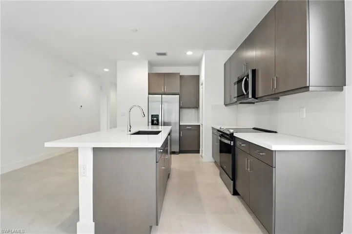 Kitchen featuring stainless steel appliances, a kitchen island with sink, dark brown cabinetry, recessed lighting, and light countertops