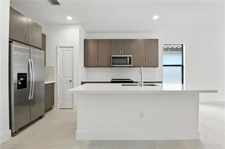 Kitchen featuring appliances with stainless steel finishes, light countertops, dark brown cabinets, an island with sink, and recessed lighting