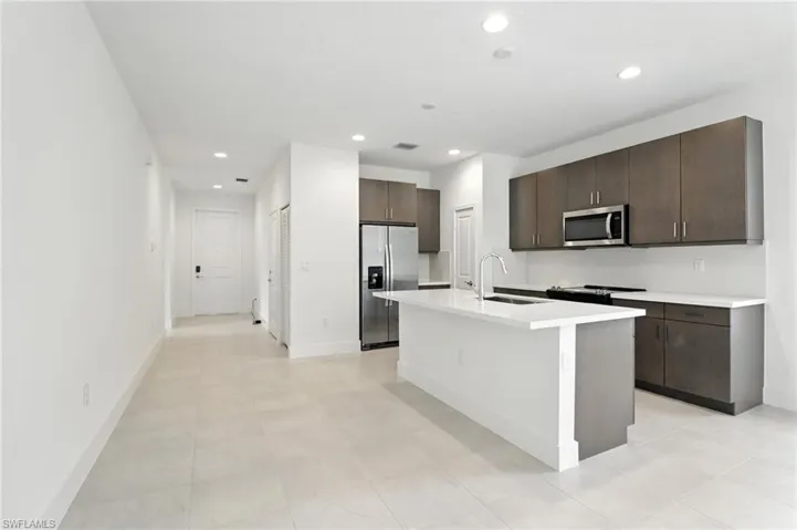 Kitchen featuring stainless steel appliances, dark brown cabinetry, recessed lighting, light countertops, and an island with sink