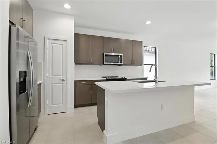 Kitchen featuring stainless steel appliances, dark brown cabinetry, light countertops, an island with sink, and recessed lighting