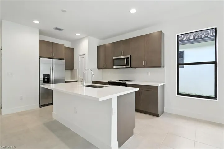 Kitchen featuring appliances with stainless steel finishes, dark brown cabinetry, light countertops, recessed lighting, and a center island with sink