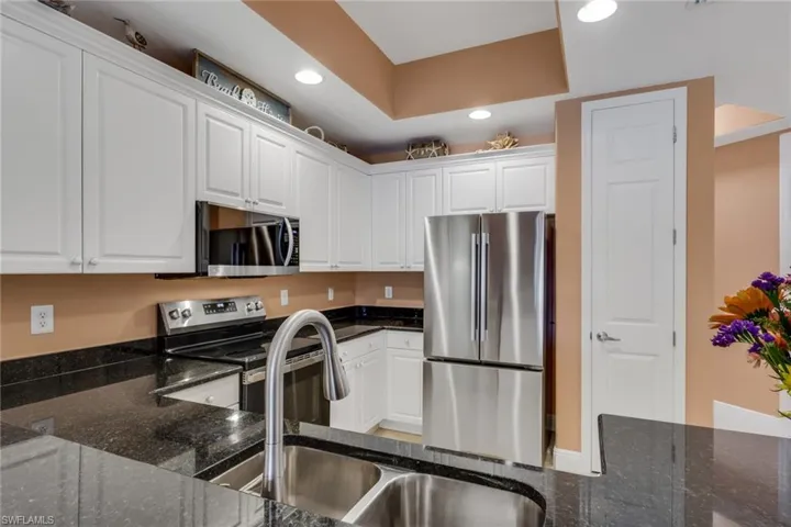 Kitchen with white cabinetry, stainless steel appliances, dark stone counters, and recessed lighting