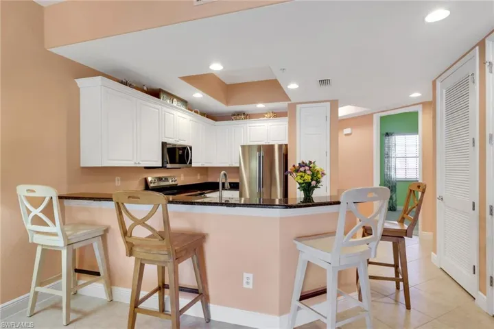 Kitchen featuring a breakfast bar area, white cabinetry, stainless steel appliances, dark stone counters, and a peninsula