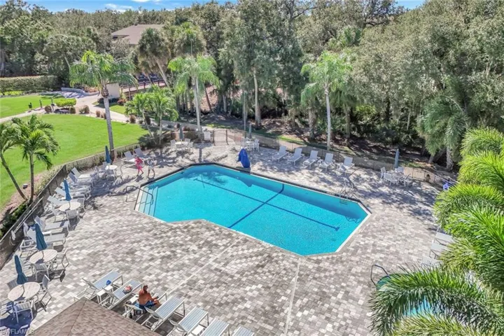 Community pool with a patio area, view of scattered trees, and outdoor dining area