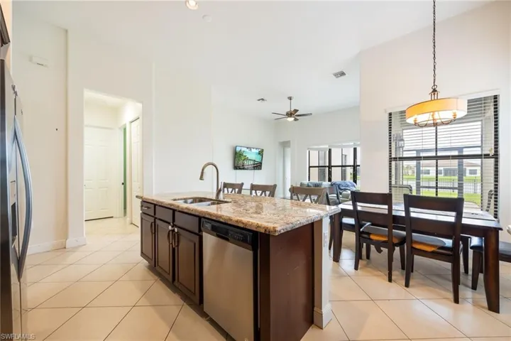 Kitchen with an island with sink, stainless steel appliances, dark wood finish cabinetry, light stone counters, and light tile patterned floors