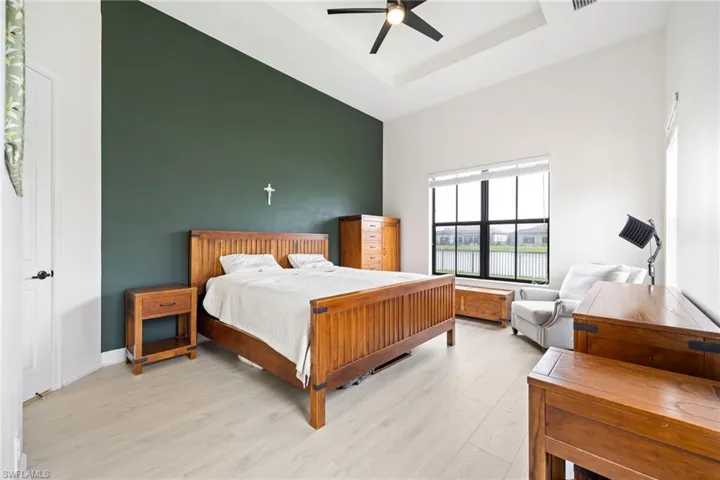 Bedroom with light wood-style floors, a ceiling fan, and a tray ceiling
