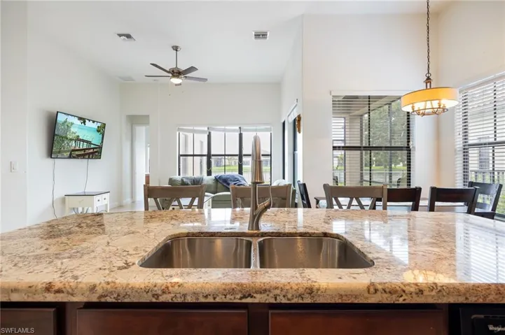 Kitchen with light stone countertops, open floor plan, hanging light fixtures, a ceiling fan, and a high ceiling