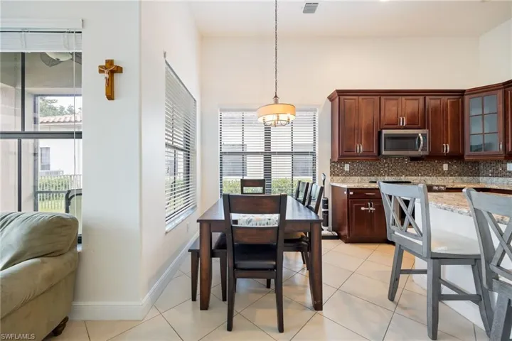 Kitchen featuring light tile patterned floors, light stone countertops, glass fronted cabinets, stainless steel microwave, and hanging light fixtures
