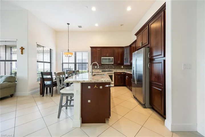 Kitchen featuring stainless steel appliances, a breakfast bar, glass insert cabinets, hanging light fixtures, and tasteful backsplash