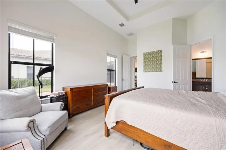Bedroom featuring a high ceiling, light wood finished floors, ensuite bathroom, and a ceiling fan