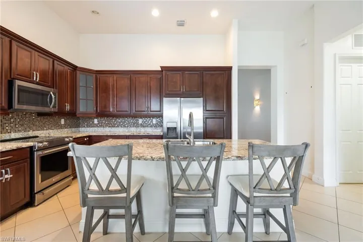 Kitchen with stainless steel appliances, a kitchen bar, glass insert cabinets, backsplash, and recessed lighting