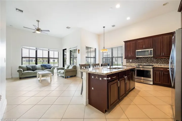 Kitchen with a breakfast bar area, stainless steel appliances, light stone counters, open floor plan, and an island with sink