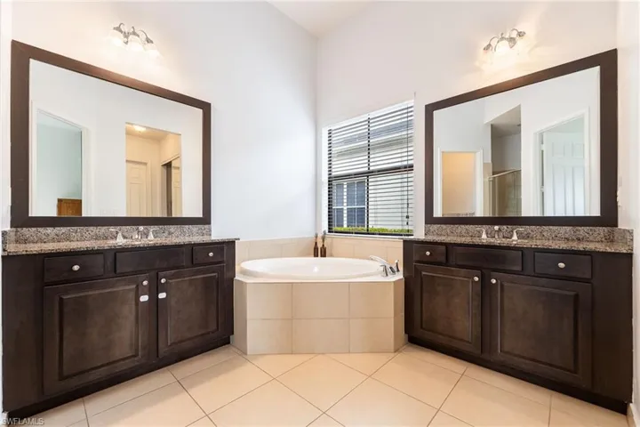 Full bathroom featuring light tile patterned flooring, a garden tub, two vanities, and a stall shower