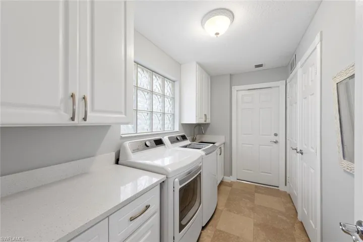 Washroom with washing machine and dryer, visible vents, a sink, and cabinet space