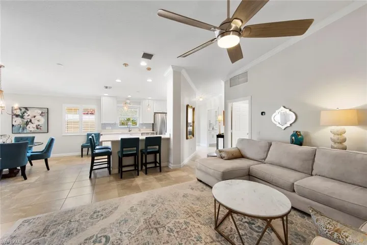 Living room featuring ceiling fan with notable chandelier, baseboards, visible vents, and crown molding