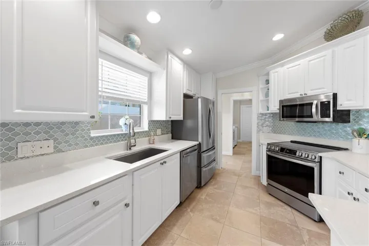 Kitchen featuring white cabinets, backsplash, stainless steel appliances, and a sink