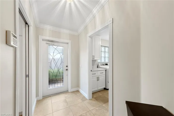 Entryway with washer / dryer, light tile patterned flooring, baseboards, and ornamental molding