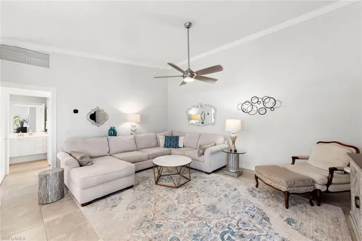 Living room with light tile patterned flooring, baseboards, visible vents, a ceiling fan, and ornamental molding