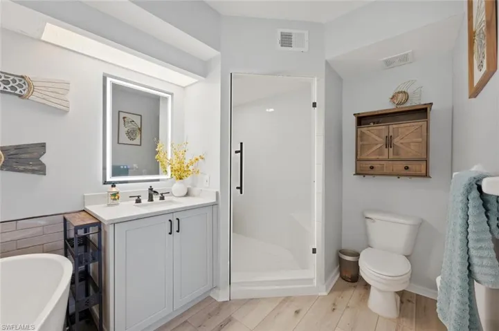 Full bathroom with a soaking tub, a shower stall, vanity, and light wood-style floors
