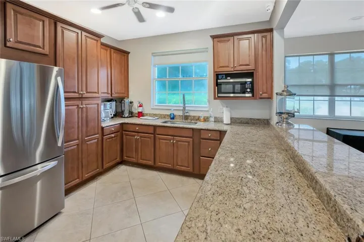 Kitchen featuring stainless steel appliances, light stone counters, wood finish cabinetry, and ceiling fan