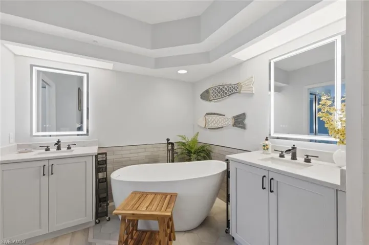Bathroom featuring two vanities, a wainscoted wall, tile walls, a freestanding bath, and light tile patterned flooring