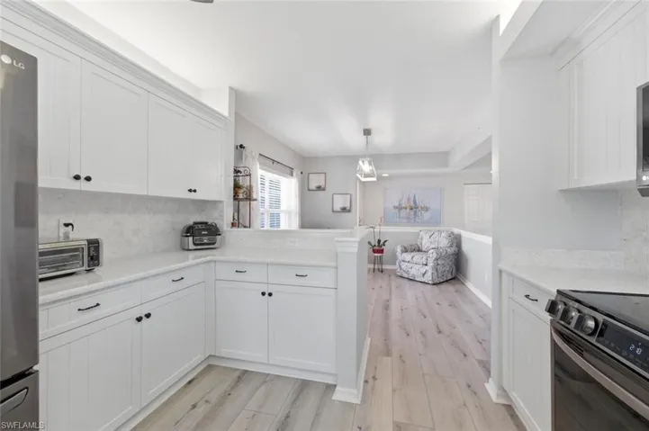 Kitchen with decorative backsplash, light wood finished floors, a peninsula, white cabinetry, and stainless steel appliances