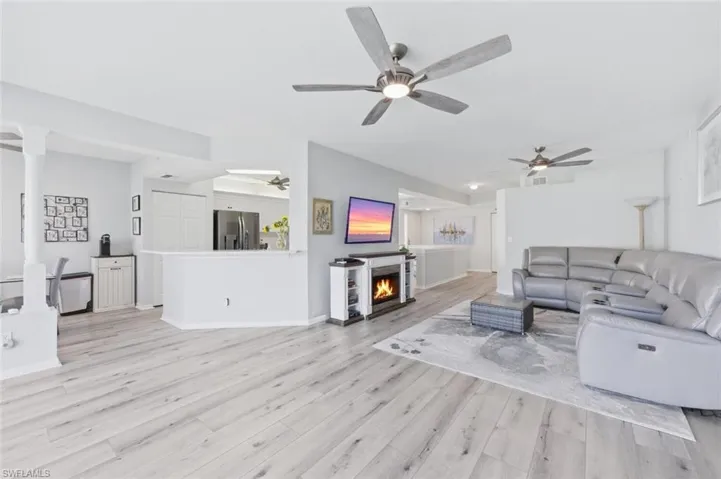 Living area with a warm lit fireplace, light wood-style flooring, and ceiling fan