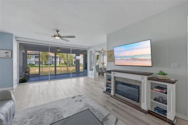 Living room featuring ceiling fan, light wood-type flooring, and a glass covered fireplace