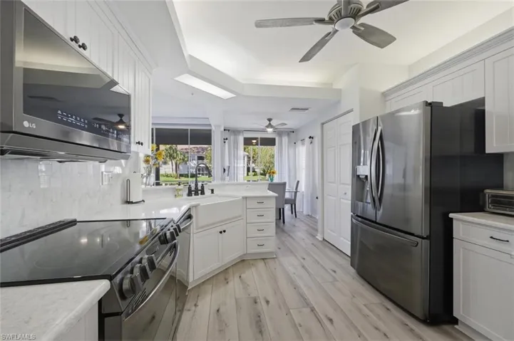 Kitchen with stainless steel appliances, white cabinetry, light wood finished floors, a peninsula, and light stone counters