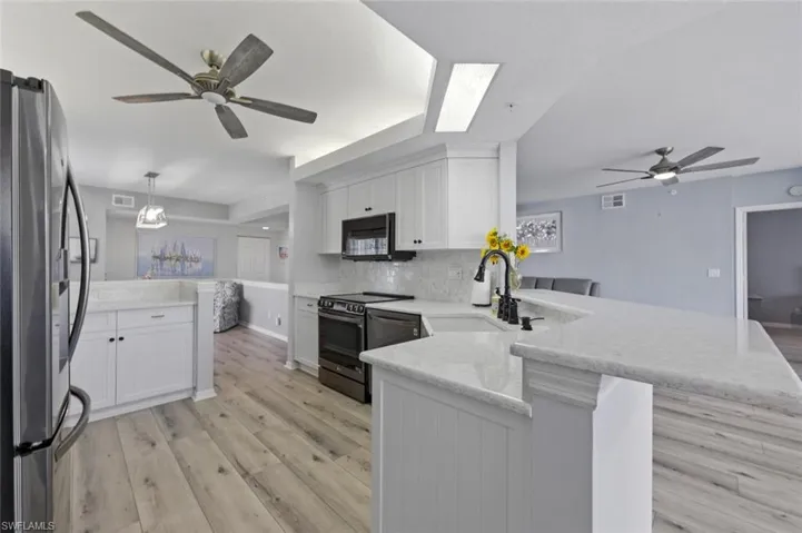 Kitchen with a ceiling fan, a peninsula, white cabinets, stainless steel appliances, and light wood-type flooring