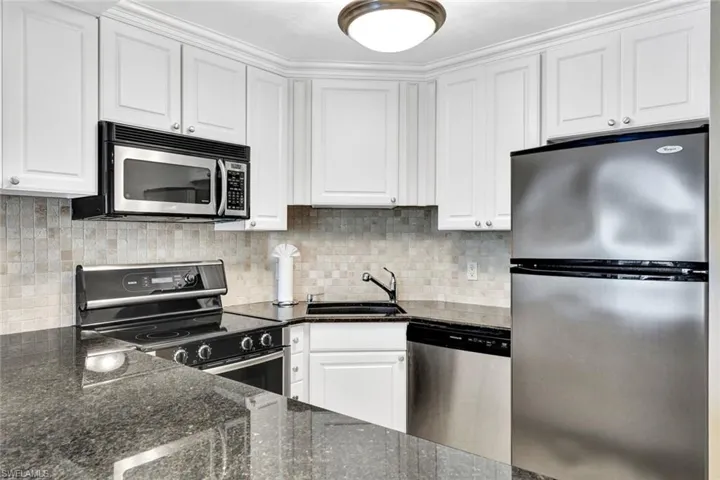 Kitchen with stainless steel appliances, dark stone counters, white cabinets, and decorative backsplash