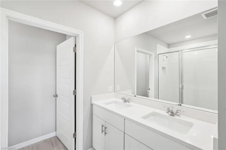 Bathroom with double vanity, toilet, a stall shower, baseboards, and recessed lighting