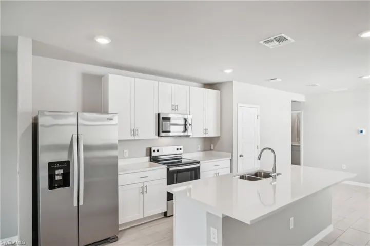 Kitchen with stainless steel appliances, a sink, white cabinets, an island with sink, and light countertops