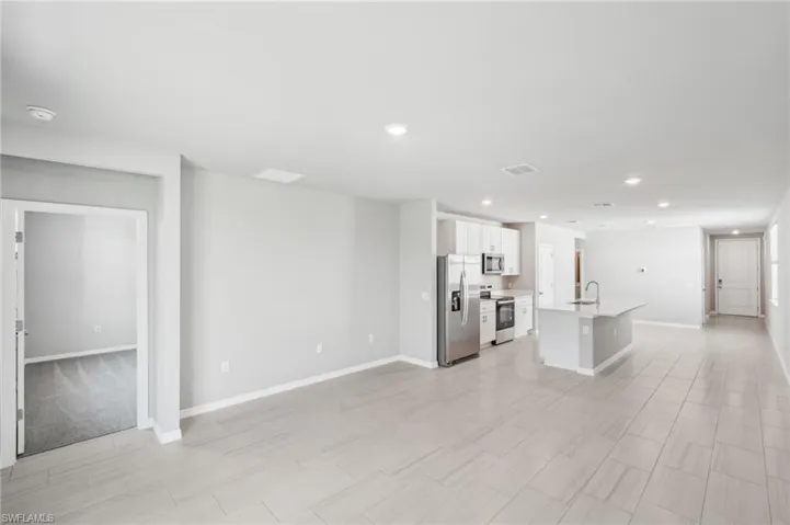 Unfurnished living room featuring a sink, recessed lighting, and baseboards