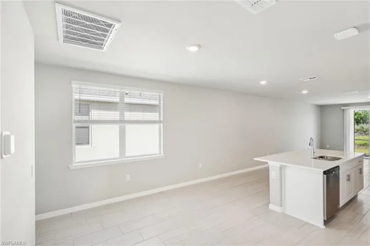 Kitchen featuring a sink, dishwasher, baseboards, light countertops, and an island with sink