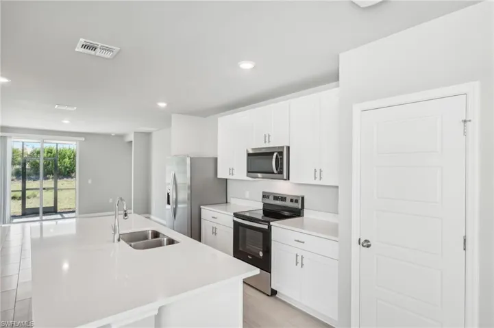 Kitchen featuring stainless steel appliances, a sink, an island with sink, white cabinetry, and recessed lighting