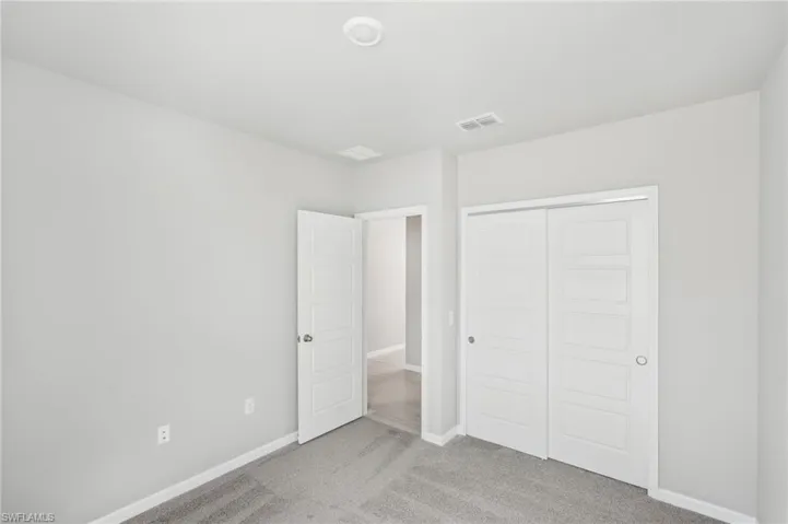 Unfurnished bedroom with light carpet, a closet, and baseboards