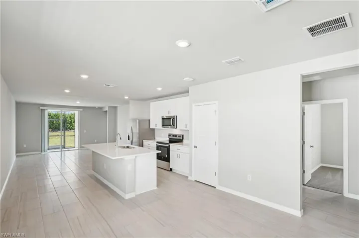 Kitchen featuring appliances with stainless steel finishes, a sink, white cabinetry, open floor plan, and a center island with sink