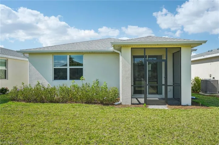 Rear view of house featuring central air condition unit, a sunroom, stucco siding, and a yard
