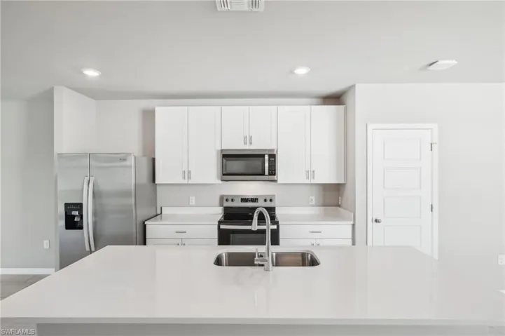 Kitchen with stainless steel appliances, a sink, light countertops, a center island with sink, and white cabinetry