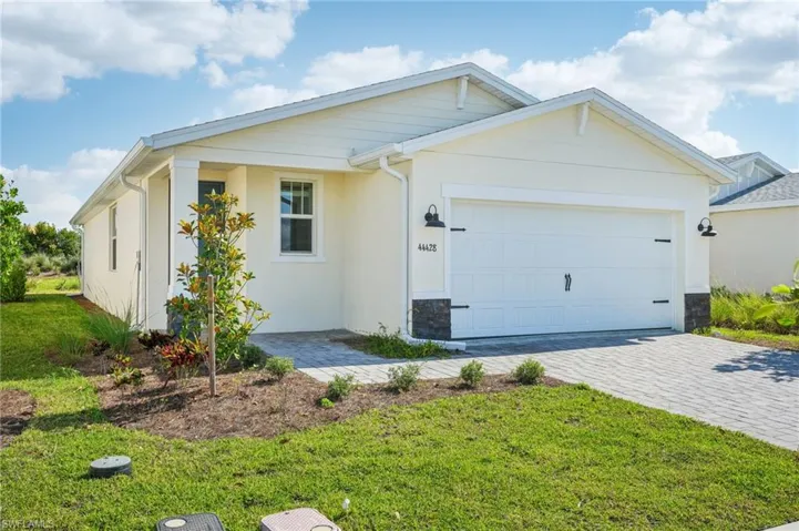 Single story home with decorative driveway, a garage, a front yard, stucco siding, and stone siding