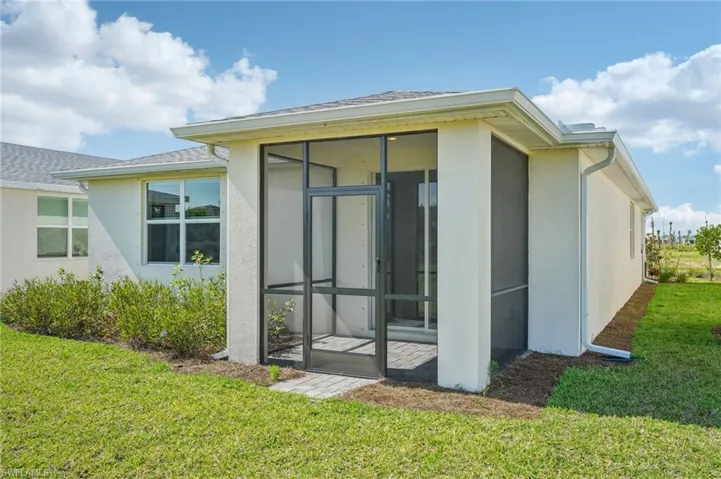 Back of property with a sunroom, a lawn, and stucco siding