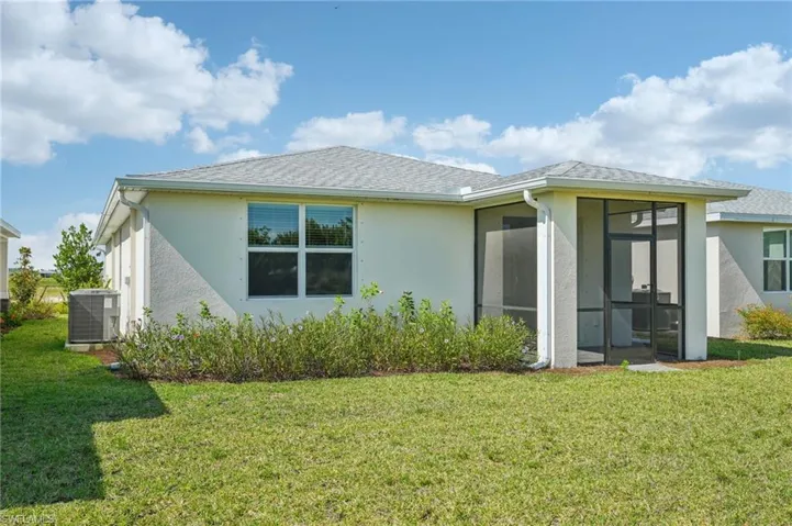 Rear view of property featuring cooling unit, a sunroom, a lawn, and stucco siding