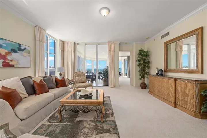 Carpeted living area featuring visible vents, crown molding, and plenty of natural light