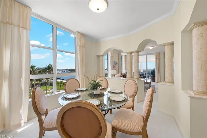 Dining area featuring ornate columns, carpet flooring, ornamental molding, and arched walkways